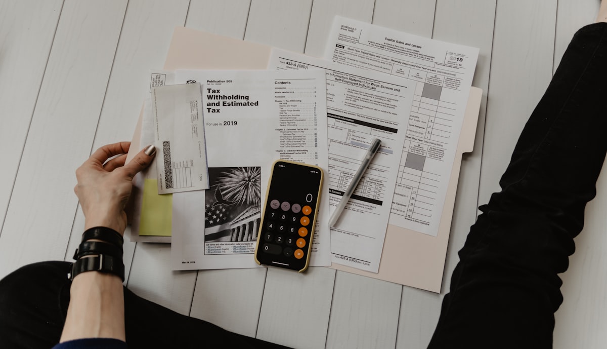 Tax forms, a calculator and a laptop laid out on a desk